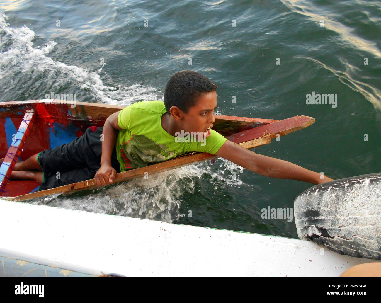 Un garçon égyptien, dans son propre petit bateau, s'accroche sur le côté d'un navire de croisière, l'attelage d'une balade sur le Nil en Egypte. Banque D'Images