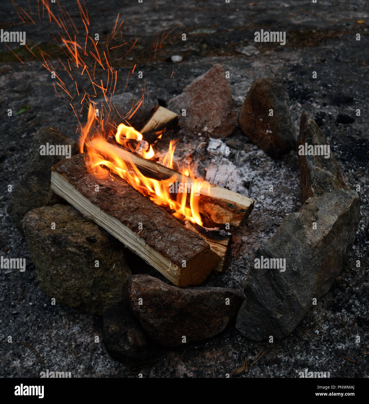 La combustion d'un feu sur un rivage rocailleux au crépuscule avec des pierres disposées en cercle Banque D'Images