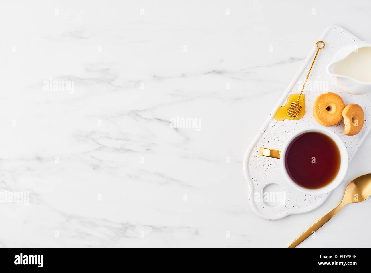 Vue de dessus de tasse de thé blanc, biscuits, lait et miel avec balancier d'or sur une assiette de service. Tasse de thé sur fond de marbre blanc. Mise à plat avec c Banque D'Images