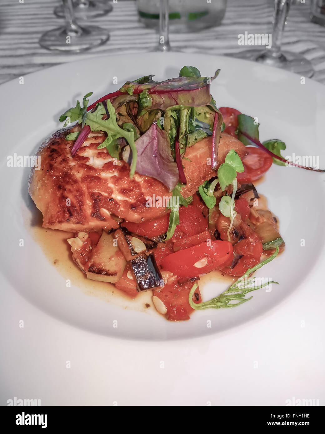 Poisson frais grillé avec tomates et autres légumes garnie de salade de légumes verts et servi dans un bol blanc peu profondes. Banque D'Images