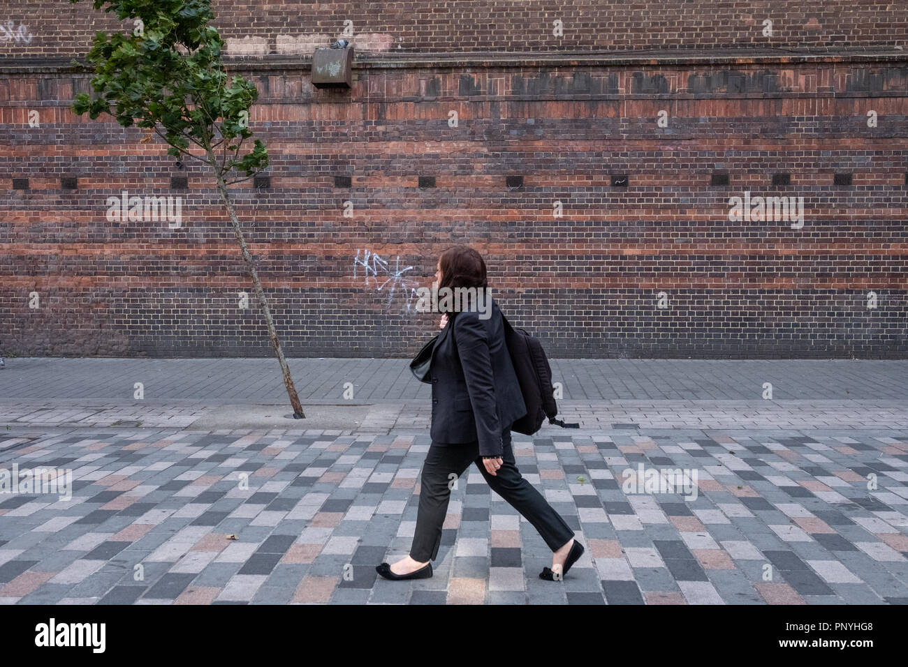 Une personne solitaire passe devant un arbre solitaire sur un jour de vent à Londres Banque D'Images
