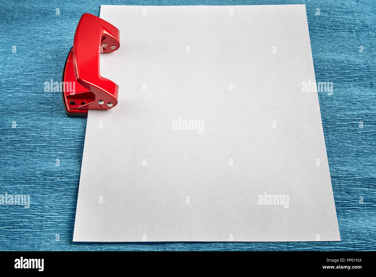 Une feuille de papier vide est serré dans la fente du Puncher, fond bleu. Banque D'Images