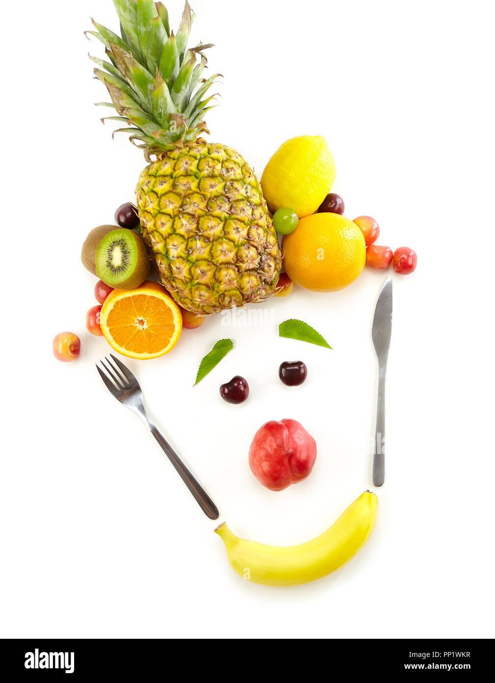 Drôle de visage composé d'un assortiment de fruits et de fourchette et couteau isolé sur fond blanc. Banque D'Images