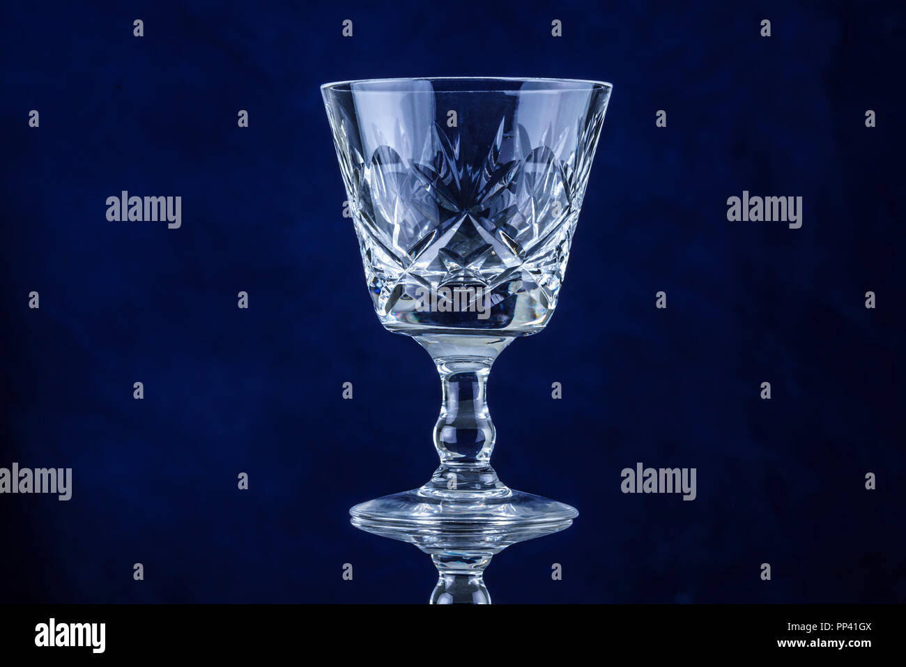 Ancien verre gobelet cristal coupe sur un fond bleu sur une surface réfléchissante Banque D'Images