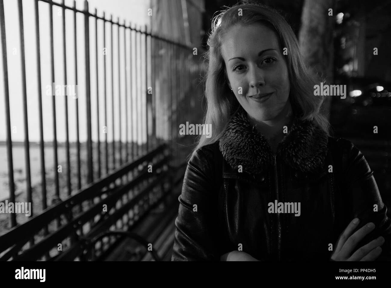 Noir et Blanc : Une jeune femme sourit pour l'appareil photo à l'extérieur à proximité d'un parc Banque D'Images