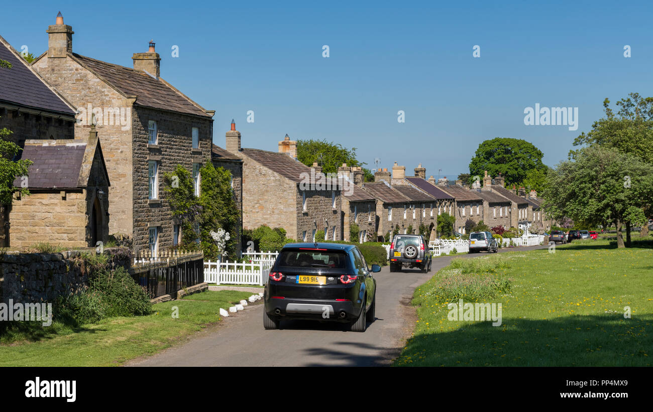 Ligne de cottages traditionnels en pierre en face du village pittoresque en communauté rurale, 4 Land Rover passant - East Witton, North Yorkshire, Angleterre, Royaume-Uni. Banque D'Images