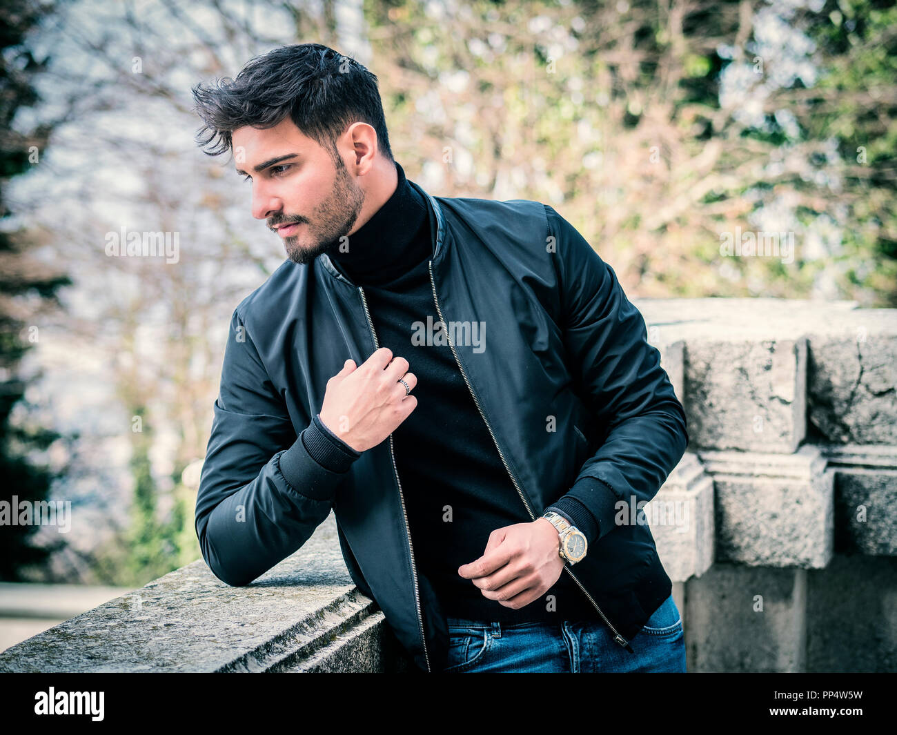 Un beau jeune homme en milieu urbain dans la ville moderne, assis, vêtu de  jeans et blouson de cuir noir Photo Stock - Alamy