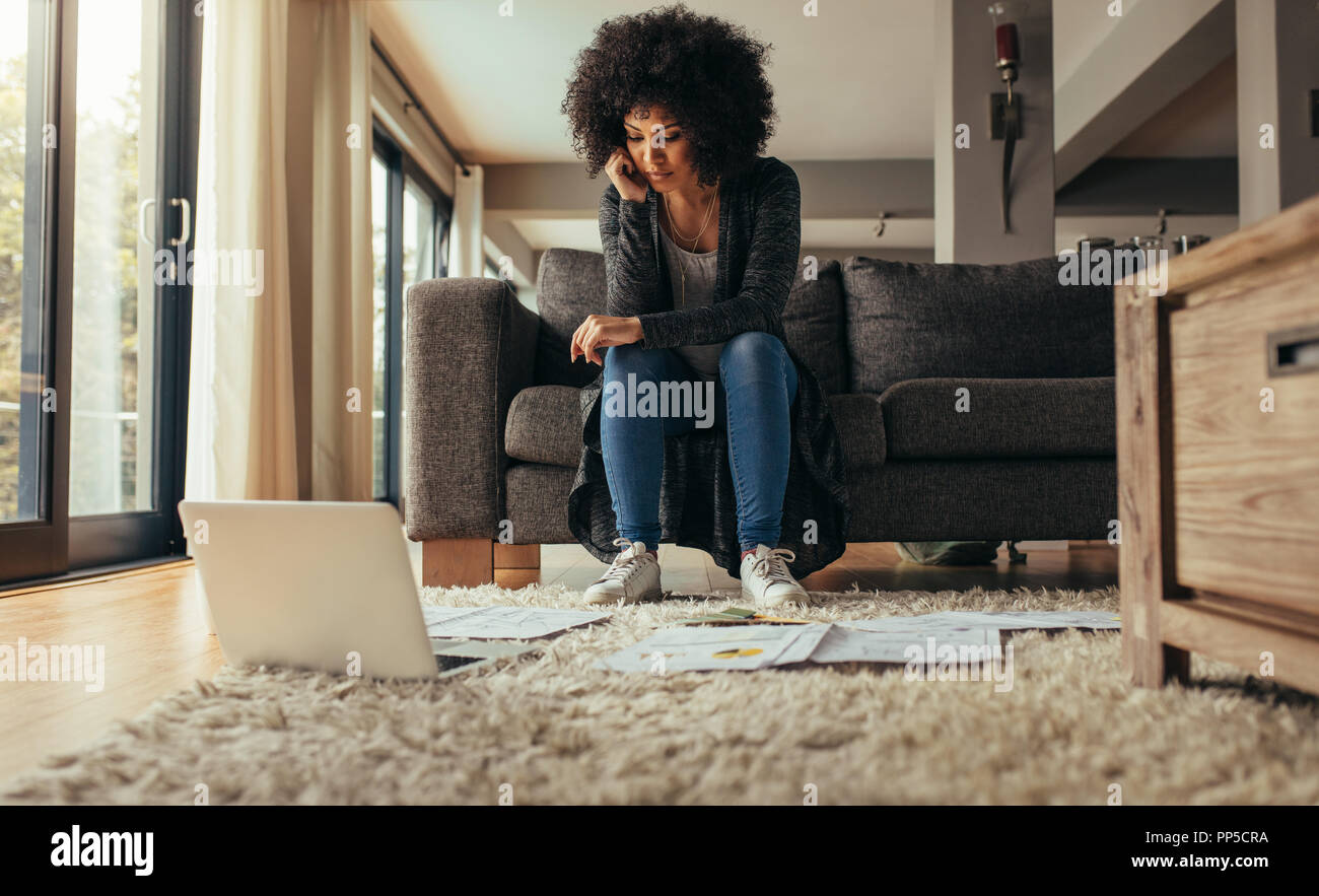 Femme assise dans canapé du salon avec quelques documents sur le plancher avec un ordinateur portable. Femme au travail sur le nouveau plan d'affaires de la maison. L'étude de femme b Banque D'Images