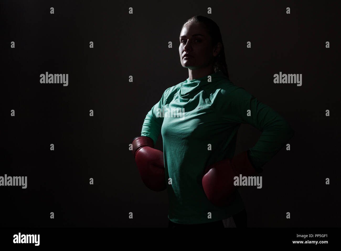 Silhouette portrait of young woman in green boxer sport wear et gants rouges et permanent à la caméra à avec les mains de taille et fier face intérieure. Banque D'Images