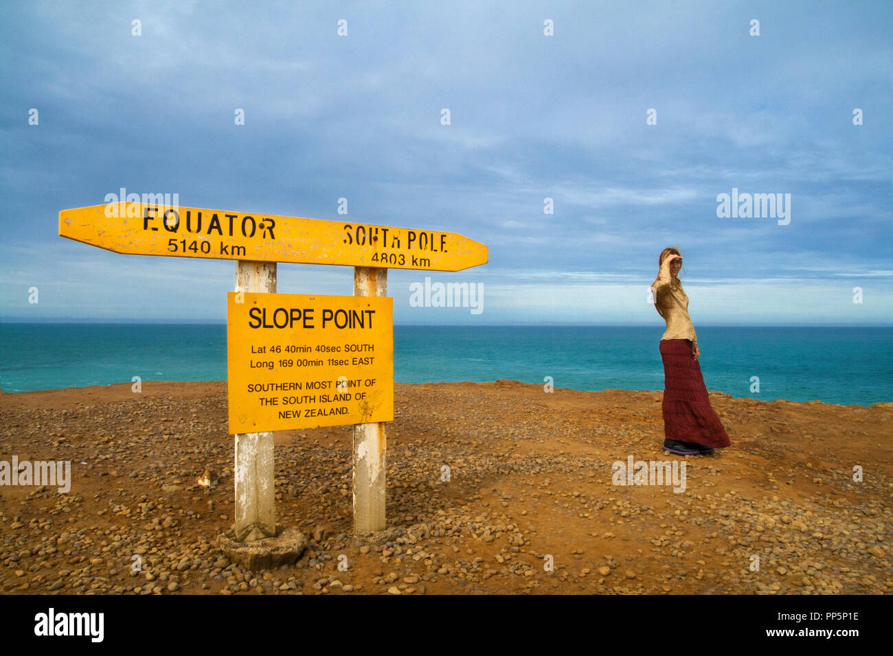 La femme de voyage debout seule sur la falaise avec vue sur l'océan Pacifique Sud, Slope point Signpost, les Catlins, île du Sud, Nouvelle-Zélande Banque D'Images