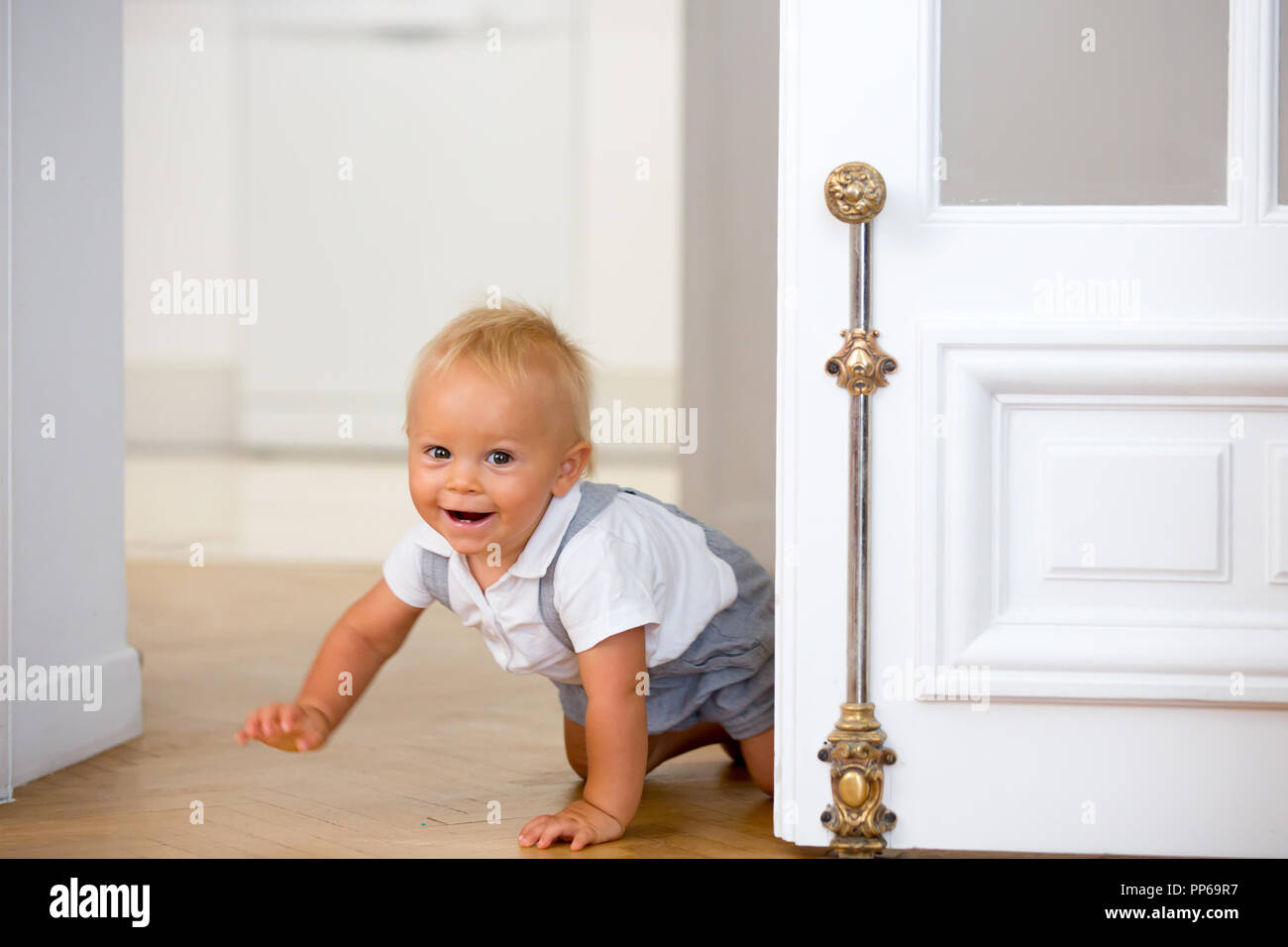 Peu mignon bébé enfant, garçon, rampant de derrière une porte à la maison Banque D'Images