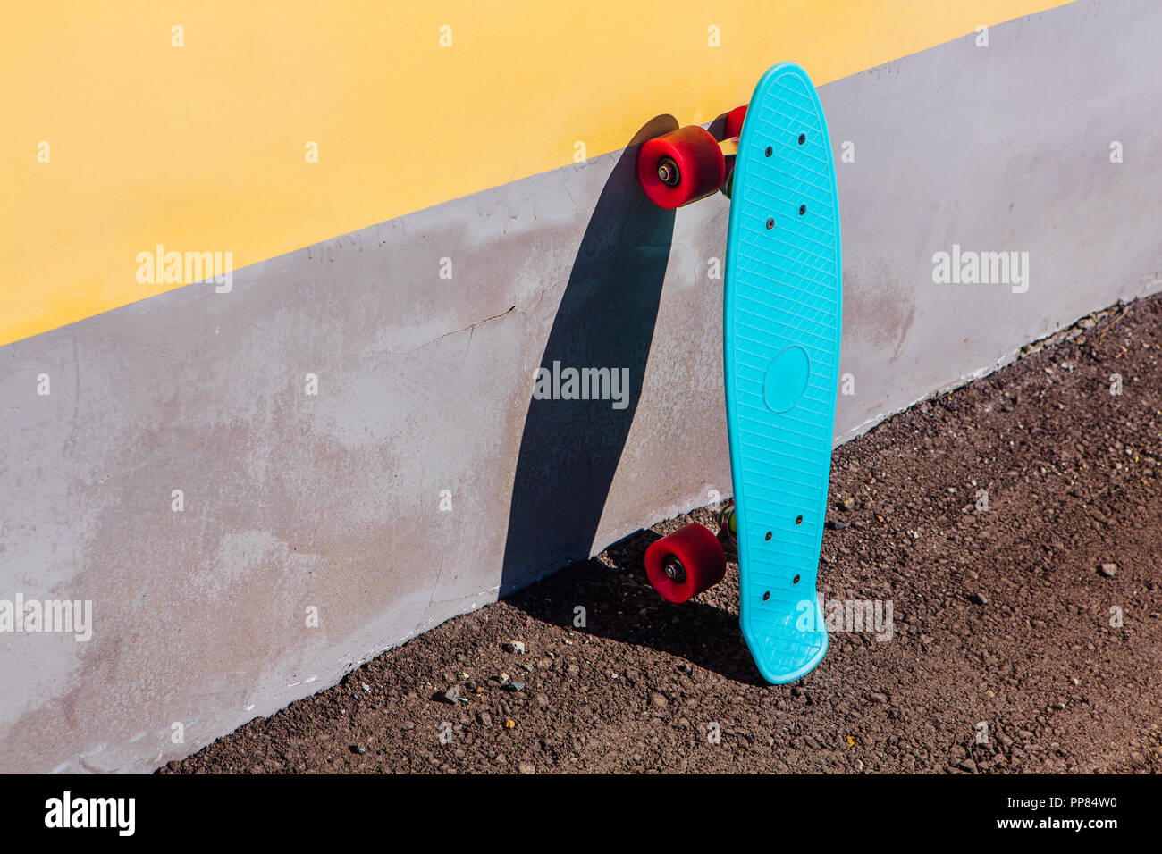 Planche à roulettes en plastique bleu avec roues conseil penny rose se dresse à côté du mur. Banque D'Images