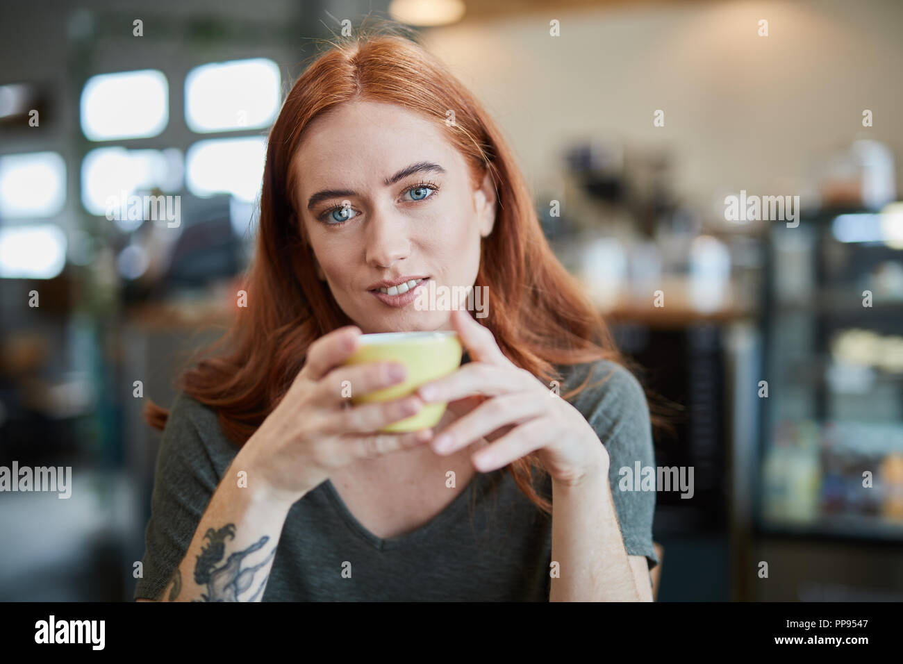 Une seule femelle, est assis dans un café de la ville avec une boisson chaude dans une tasse, looking at camera Banque D'Images