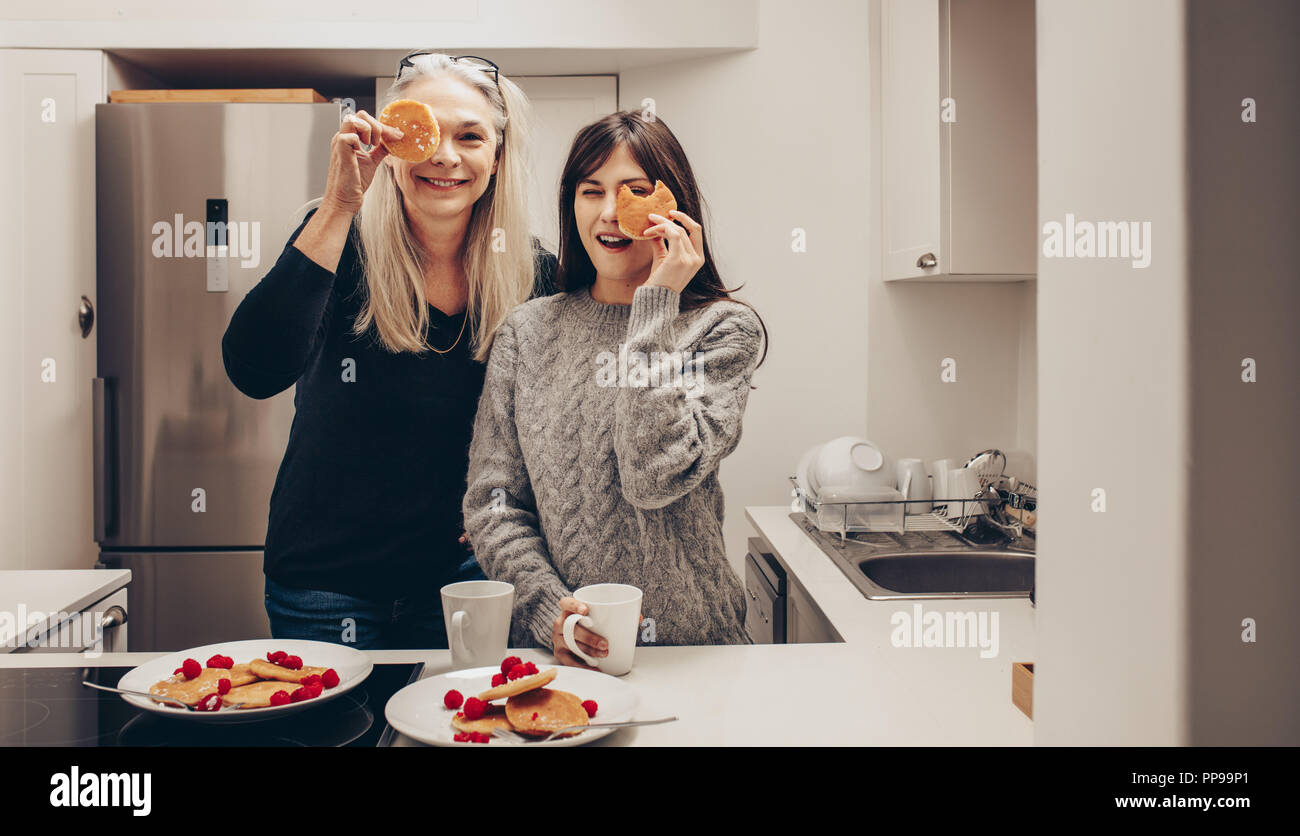 Happy mother and daughter standing dans la cuisine avec plaques plein de cookies. Deux smiling women in kitchen holding cookies devant leurs yeux. Banque D'Images