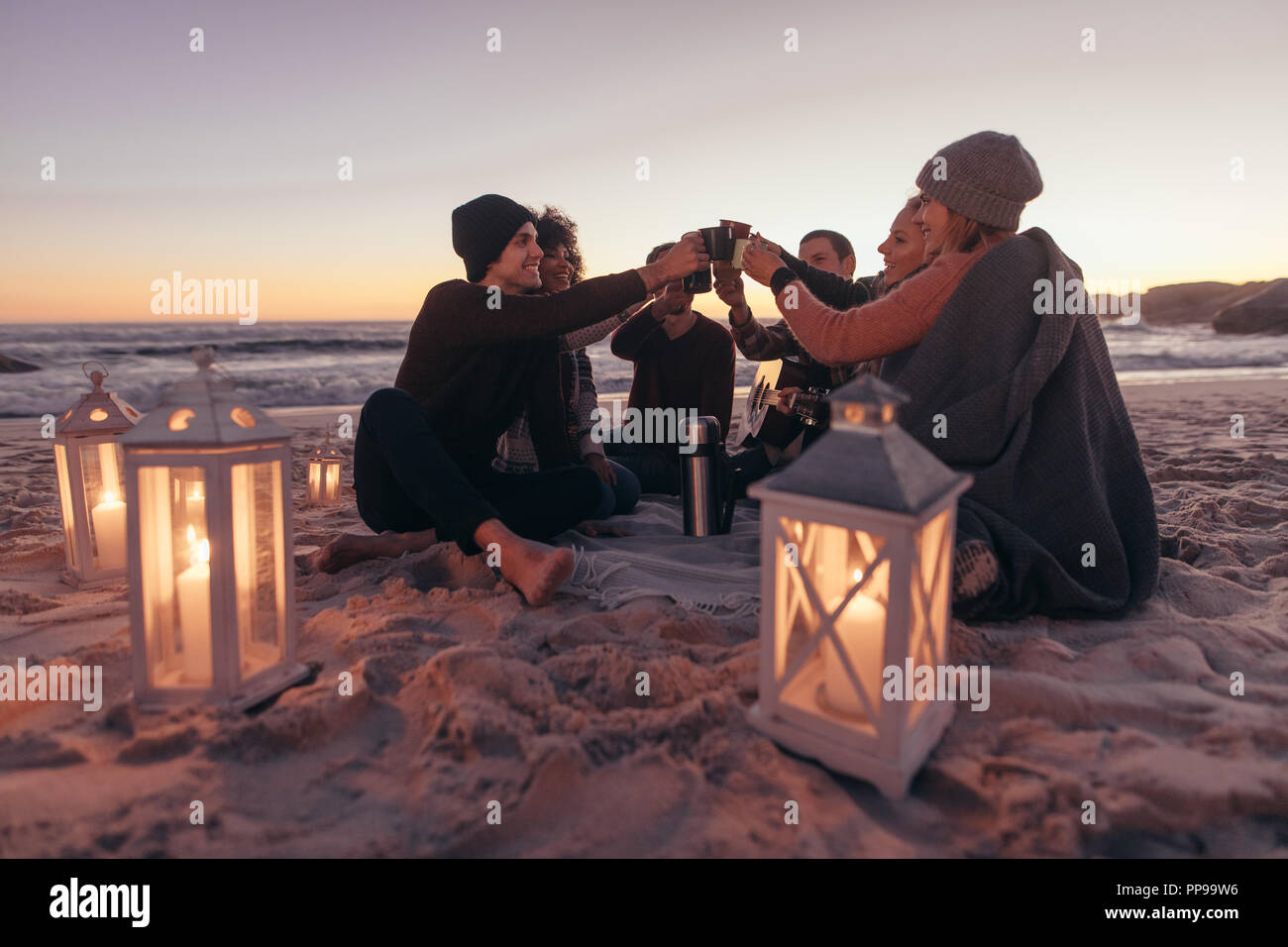 Groupe de jeunes gens assis ensemble à la plage de fonctionnement du café sur chaude soirée. Les amis à faire la fête dans la plage avec du café. Banque D'Images