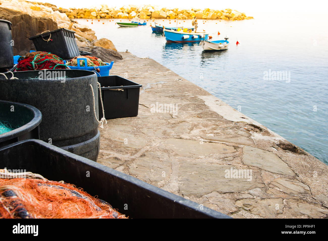 Village de pêcheurs méditerranéen quai avec tambours et les conteneurs remplis de filets de pêche avec des bateaux amarrés en arrière-plan Banque D'Images