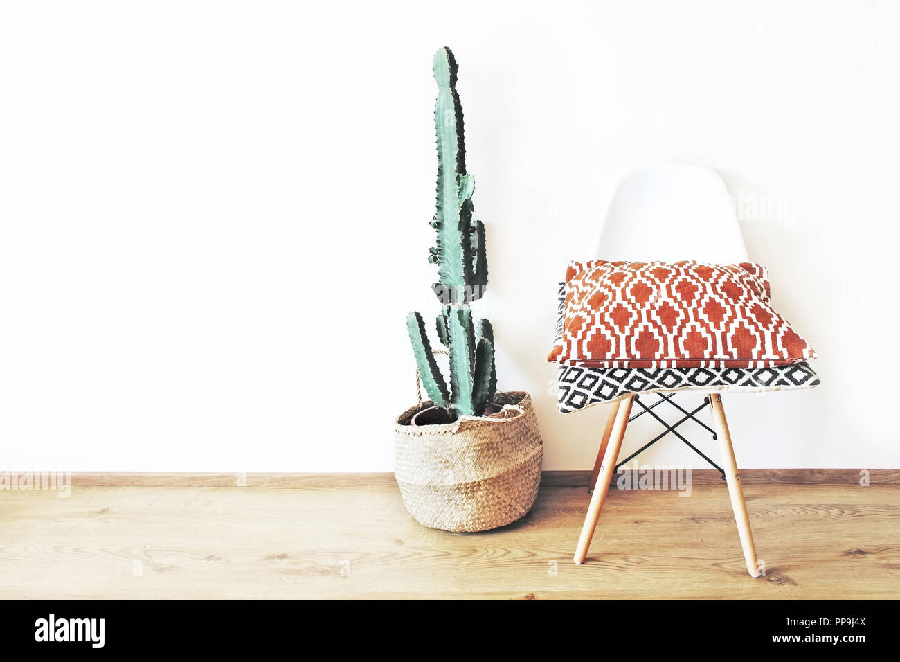 Succulent Euphorbia plante en panier de paille et unpholstered chaise moderne sur un plancher en bois de chêne. Mur Blanc arrière-plan. Les Oreillers de modèles ethniques. Éclectique contemporain home design minimal. Banque D'Images