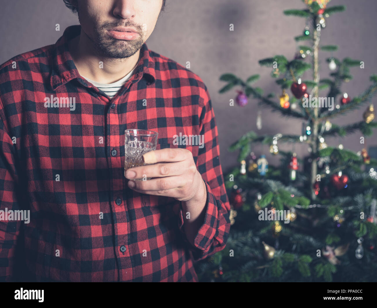 Un jeune homme triste et déprimé est un verre par l'arbre de Noël Banque D'Images