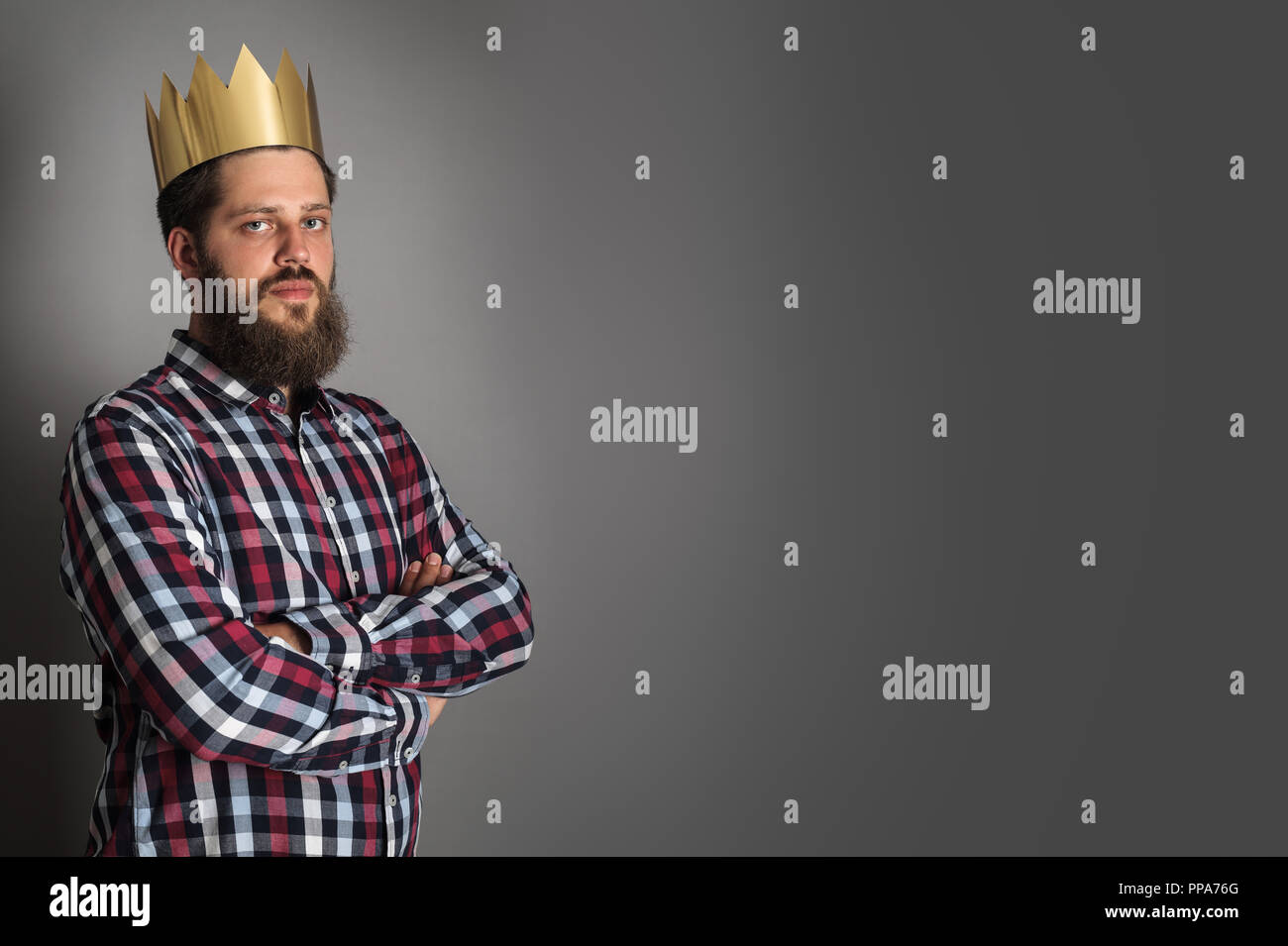 Homme barbu en couronne d'or looking at camera while standing avec bras croisés sur fond gris Banque D'Images