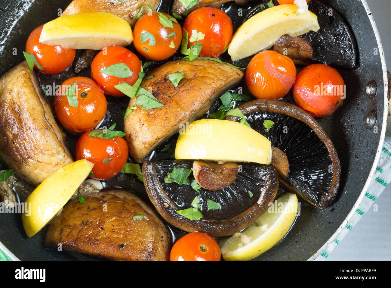 Les champignons et tomates cerises sautées étant dans une poêle peu profonde, garnie de persil frais haché et des quartiers de citron Banque D'Images