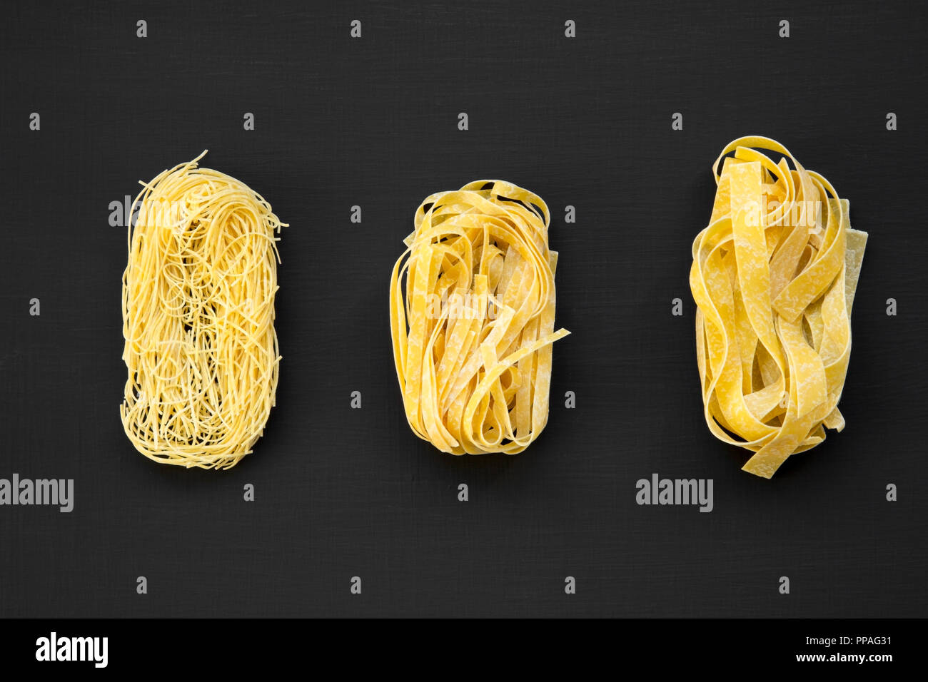 Ensemble de diverses pâtes alimentaires non cuites(fettuccine, pappardelle, tagliolini) sur la surface noire, vue du dessus. Close-up. Banque D'Images