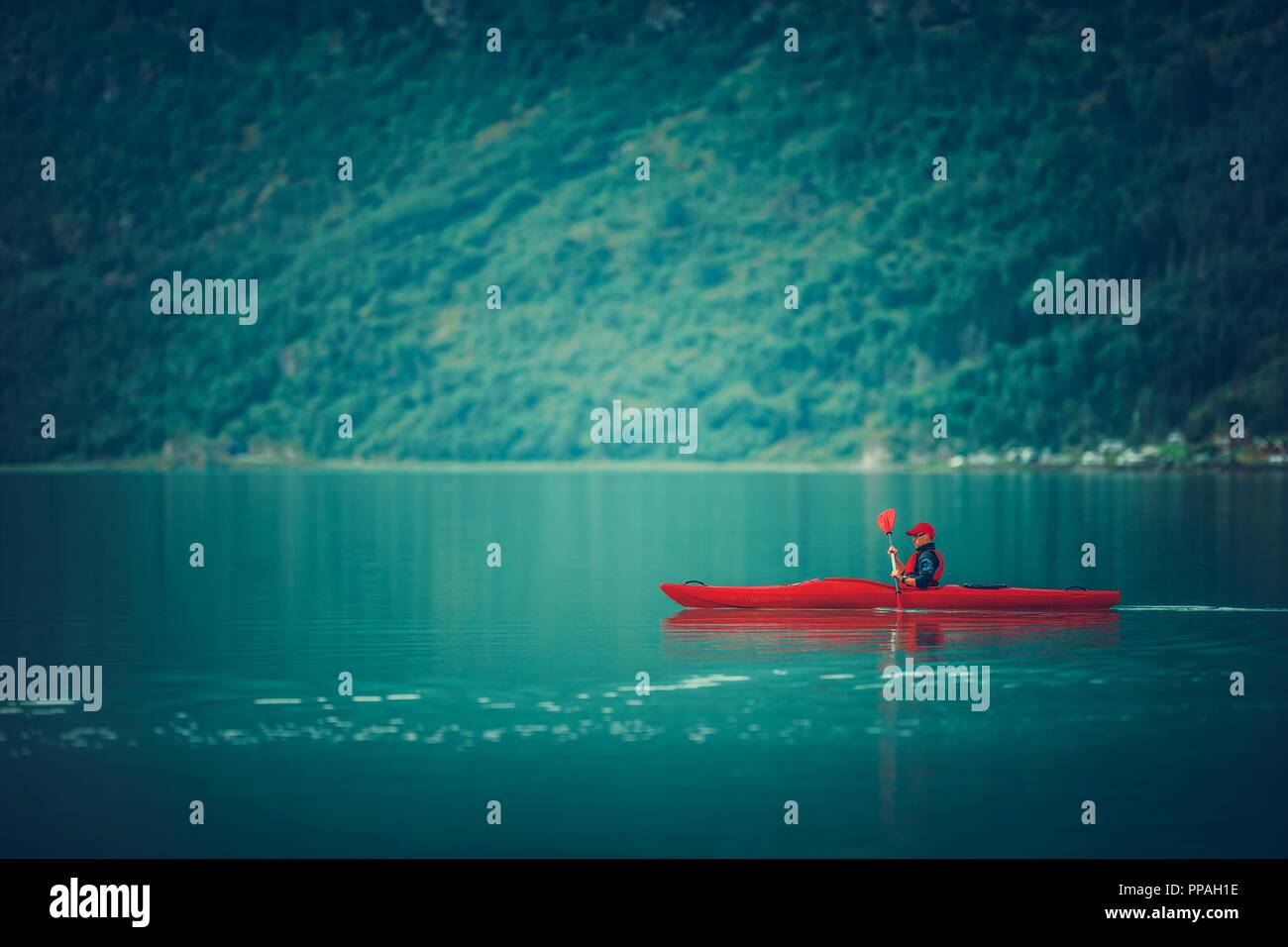 Le lac glaciaire du kayak. Young Sportsman pagayer dans le Kayak rouge. Banque D'Images