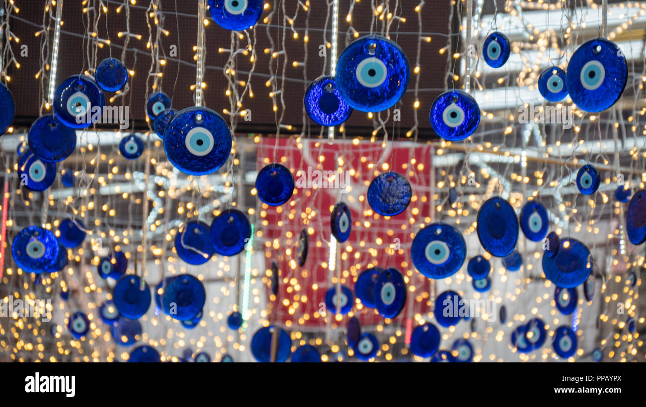 Close up des amulettes en forme d'œil bleu appelé oeil mauvais ou Nazar. Pendu sur le toit. Drapeau turc floue et les voyants sur l'arrière-plan. Banque D'Images