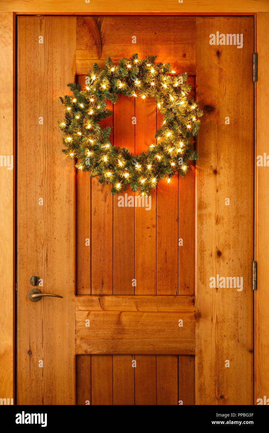 Belle couronne de evergreen éclairés sur la pendaison de porte avant en bois Accueil Historique. Simple, style rustique vacances de Noël la décoration d'intérieur. Banque D'Images