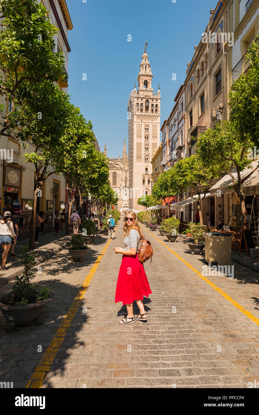 Femme avec robe rouge sur la rue, derrière la Giralda, beffroi de la Cathédrale de Séville, Cathédrale de Santa Maria de la Sede, Séville Banque D'Images