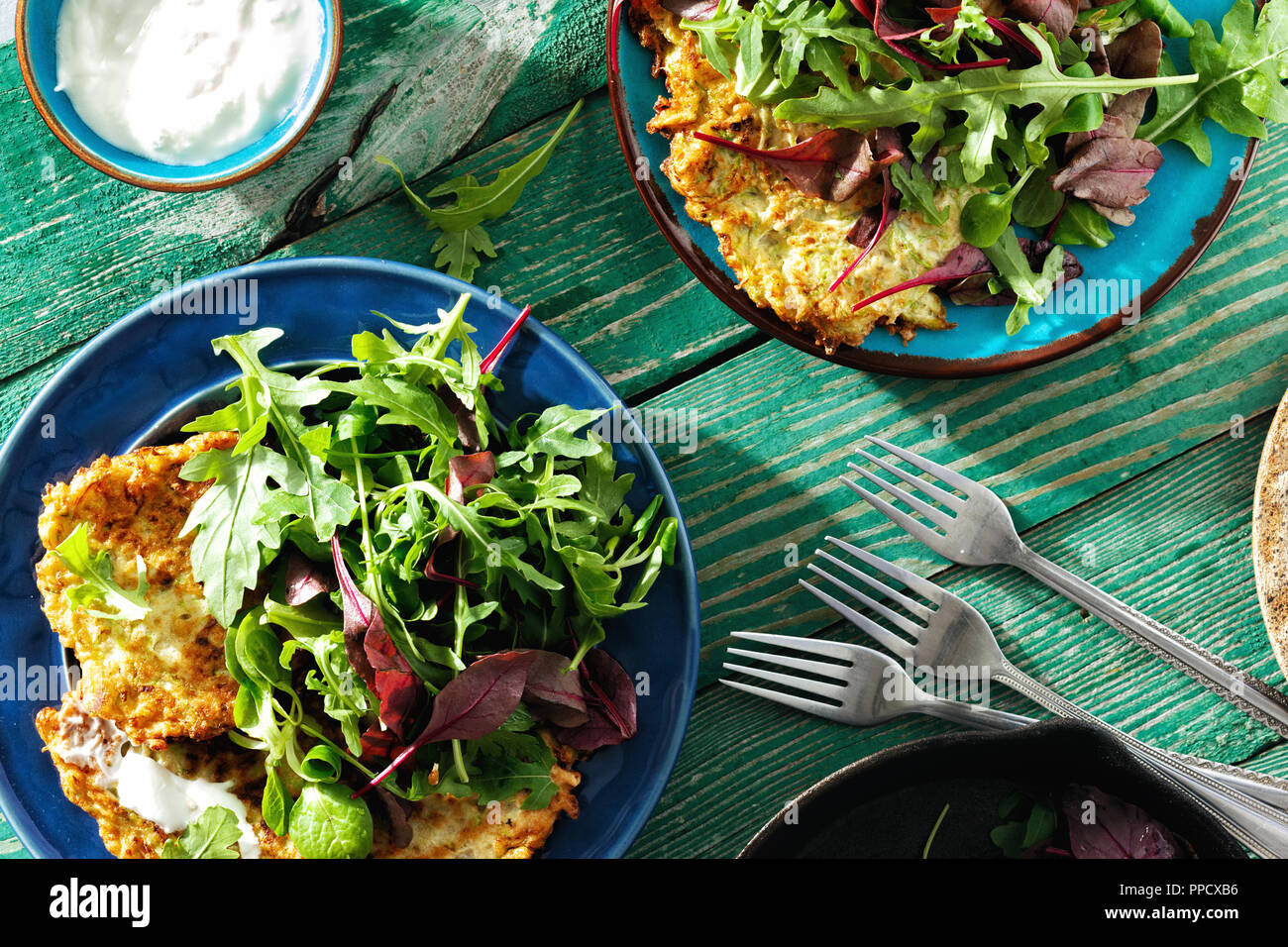 Comfort food concept. Crêpes de courgettes frites servi sur une assiette avec salade sur table en bois avec du yaourt grec vue supérieure Banque D'Images