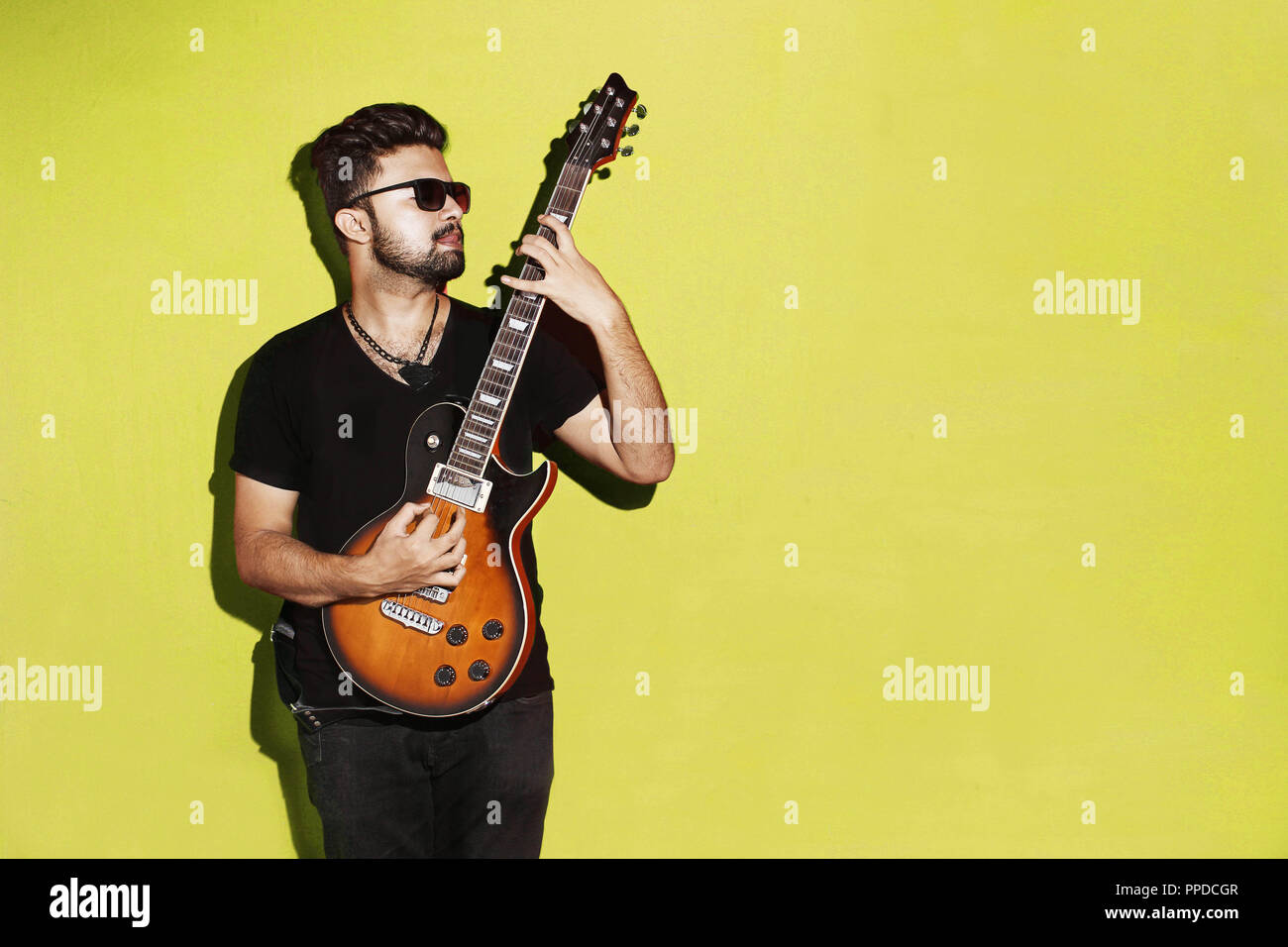 Gros plan sur un beau musicien de rock brunette, expressif et passionné, jouant de la guitare électrique sur fond jaune Banque D'Images
