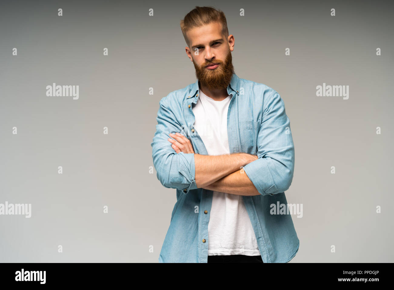 Portrait of fashionable bel homme en jeans shirt traversant les mains et regarde la caméra. Banque D'Images