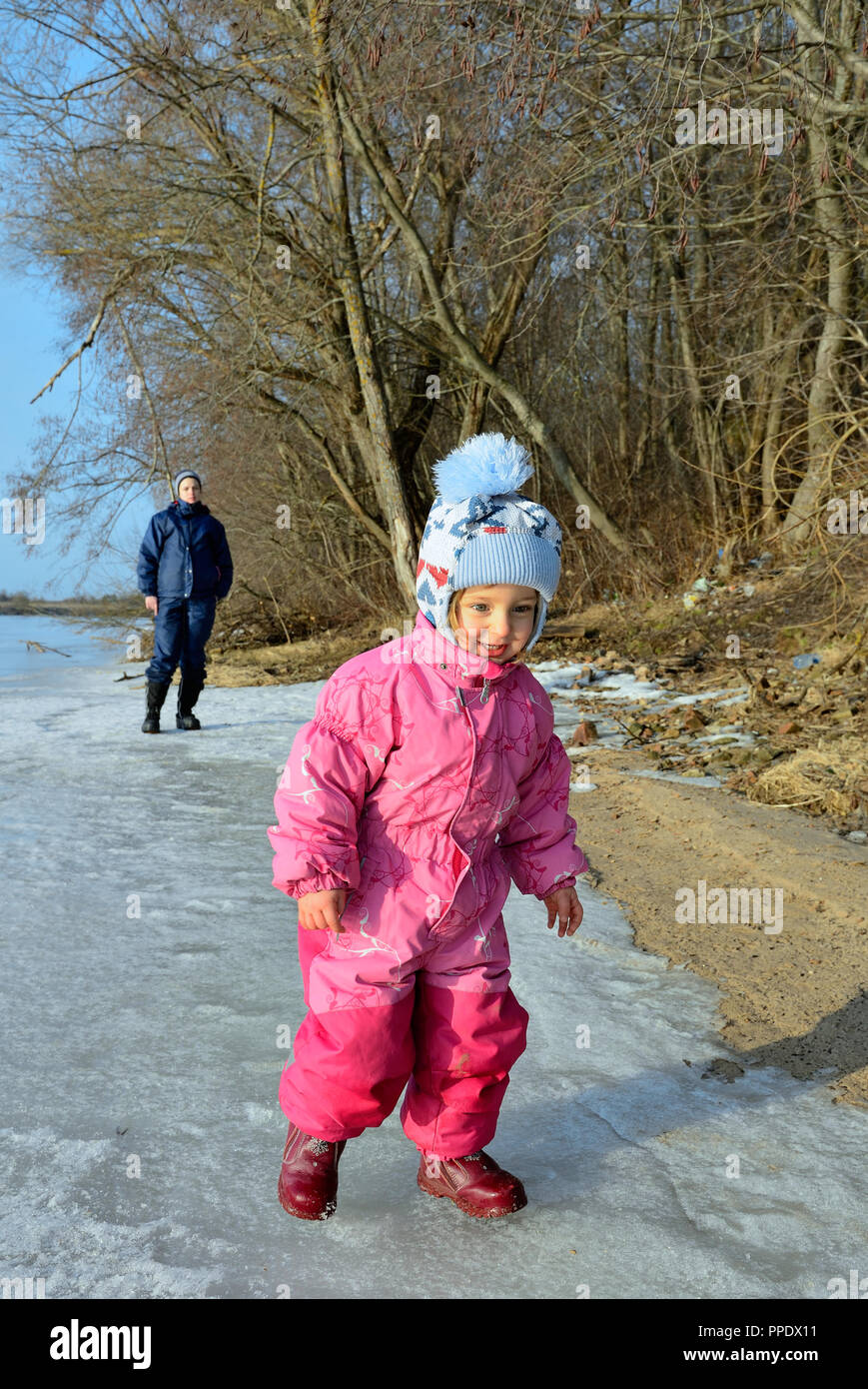 Petite fille sur la glace de rivière. yhe Jeune mère et petite fille dans la lumière du soleil sur la rive du fleuve. Au début du printemps. Banque D'Images