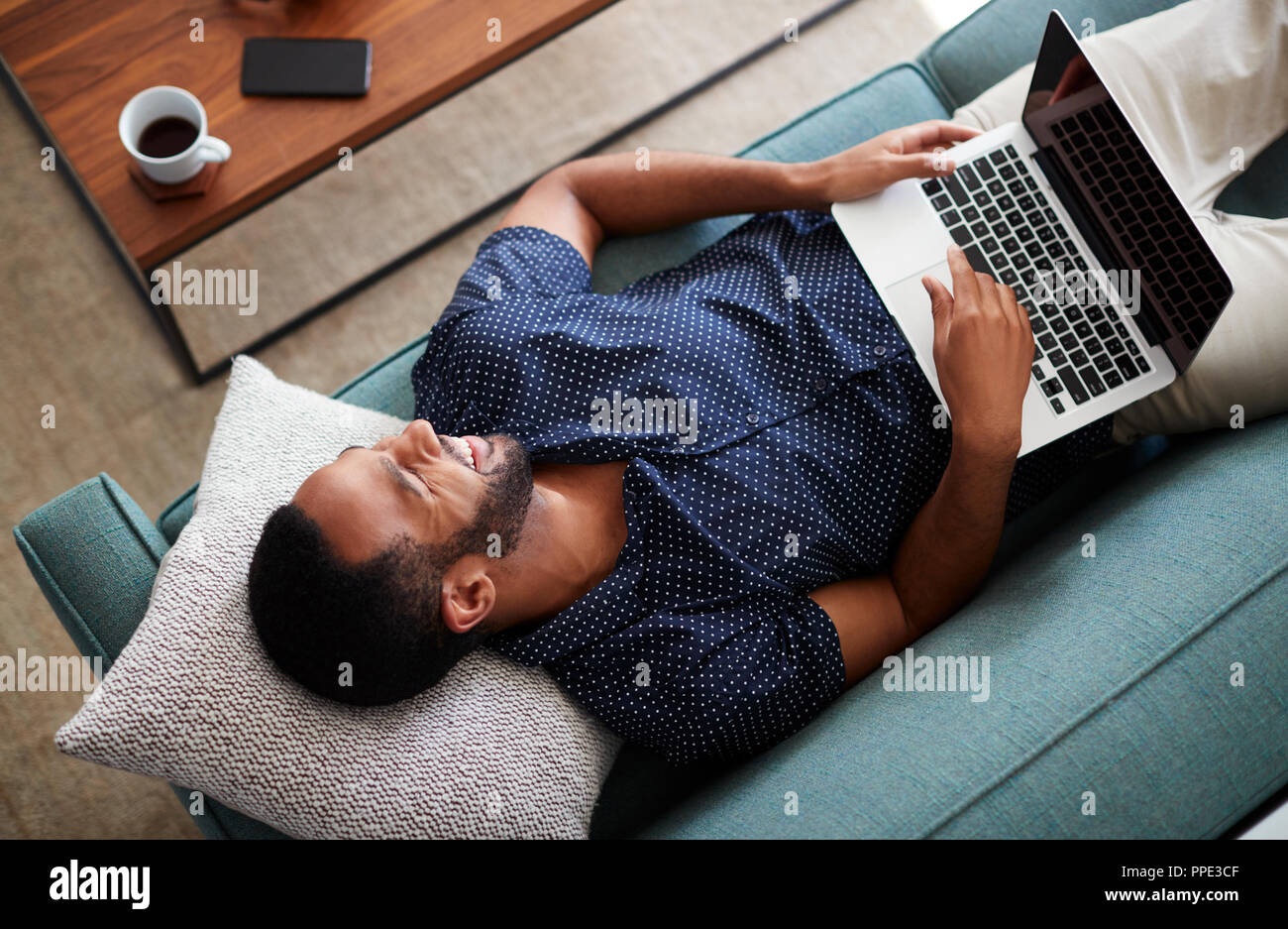 Vue supérieure de l'homme étendu sur le canapé à la maison à l'aide d'un ordinateur portable Banque D'Images Vue supérieure de l'homme étendu sur le canapé à la maison à l'aide d'un ordinateur portable Banque D'Images
