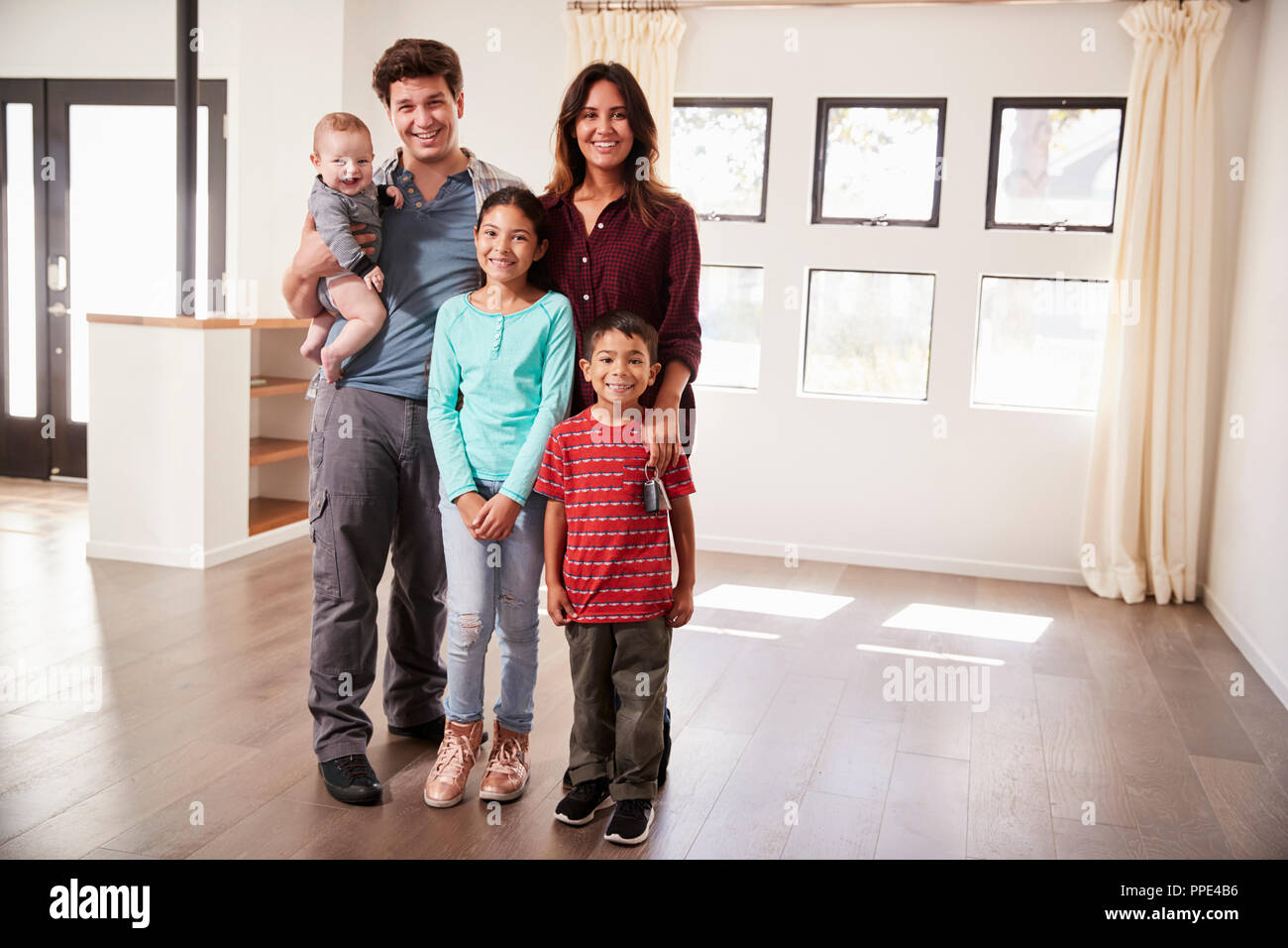 Portrait de famille heureuse avec bébé debout dans le salon vide de New Home Banque D'Images