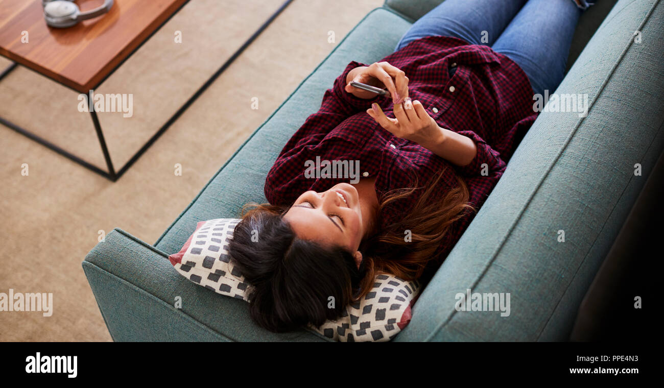 Vue de dessus de Woman Lying On Sofa At Home Using Mobile Phone Banque D'Images Vue de dessus de Woman Lying On Sofa At Home Using Mobile Phone Banque D'Images