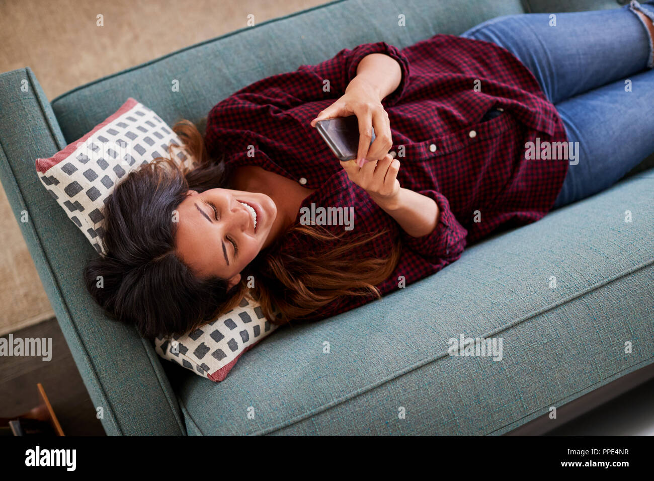 Vue de dessus de Woman Lying On Sofa At Home Using Mobile Phone Banque D'Images Vue de dessus de Woman Lying On Sofa At Home Using Mobile Phone Banque D'Images