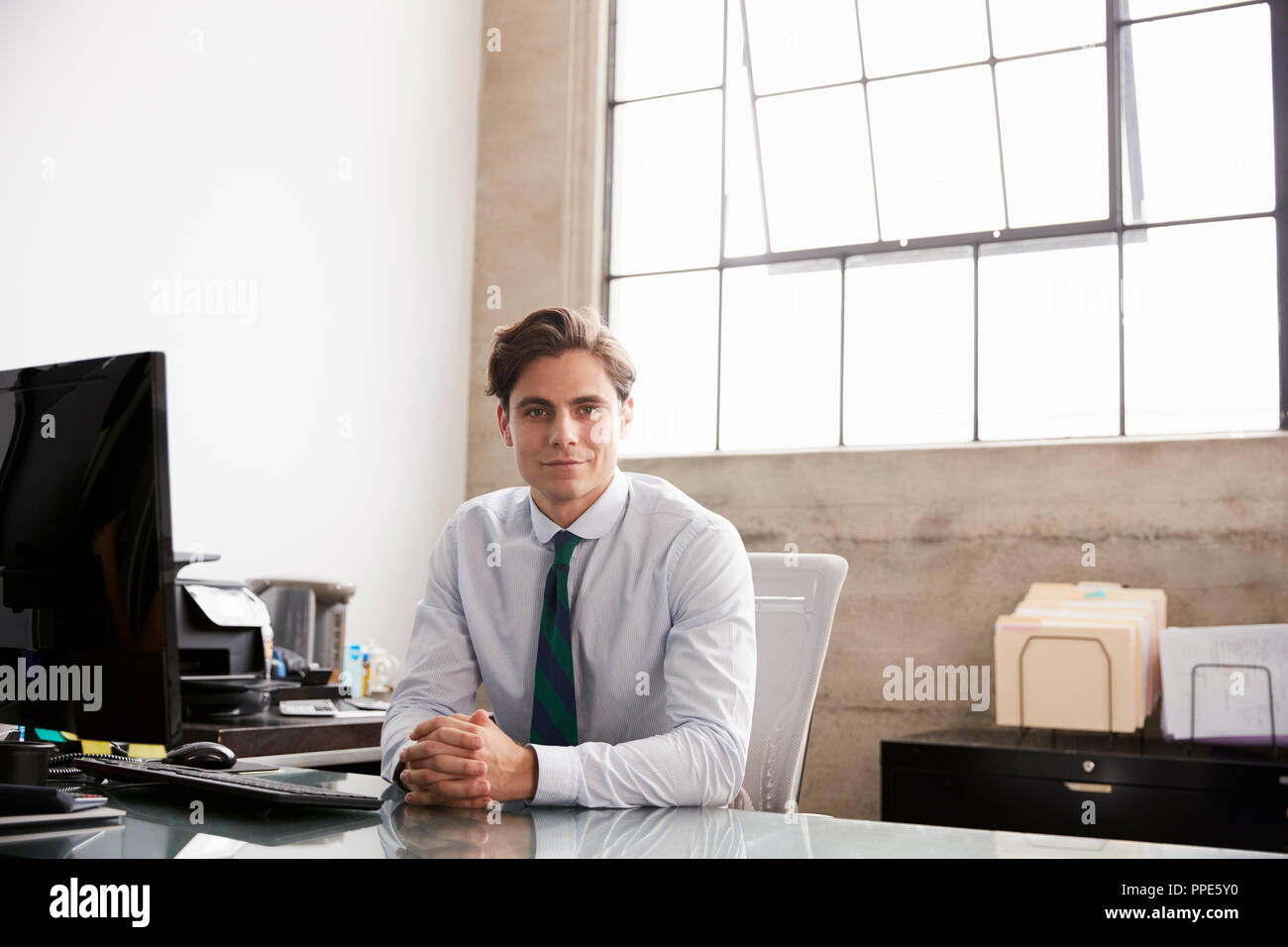 Young businessman sitting at office desk smiling to camera Banque D'Images