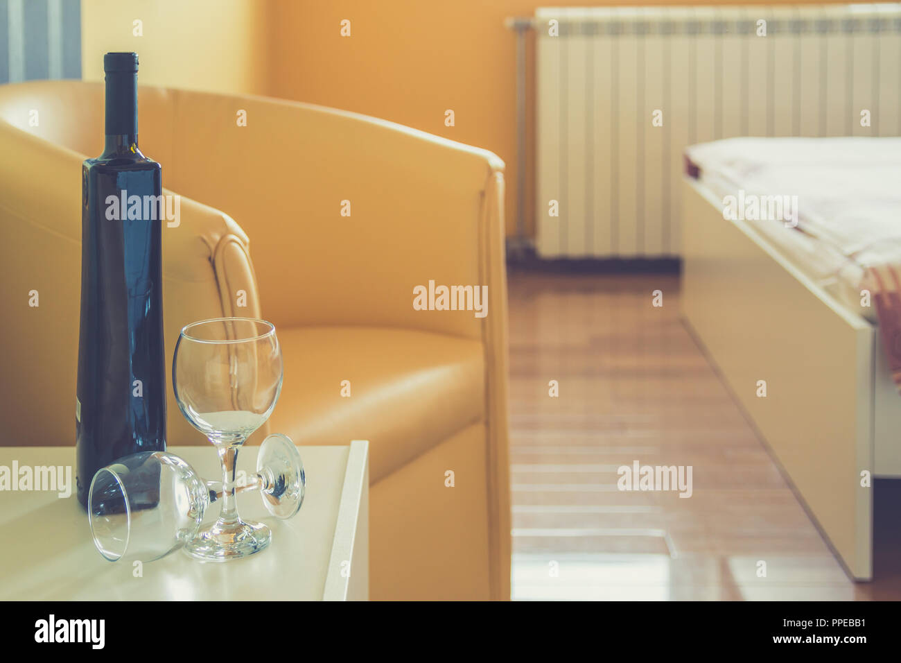 Bouteille de vin rouge et deux verres sur la table de nuit à côté du fauteuil et lit double dans la chambre à coucher moderne. Ensemble romantique pour la Saint-Valentin ou anni Banque D'Images