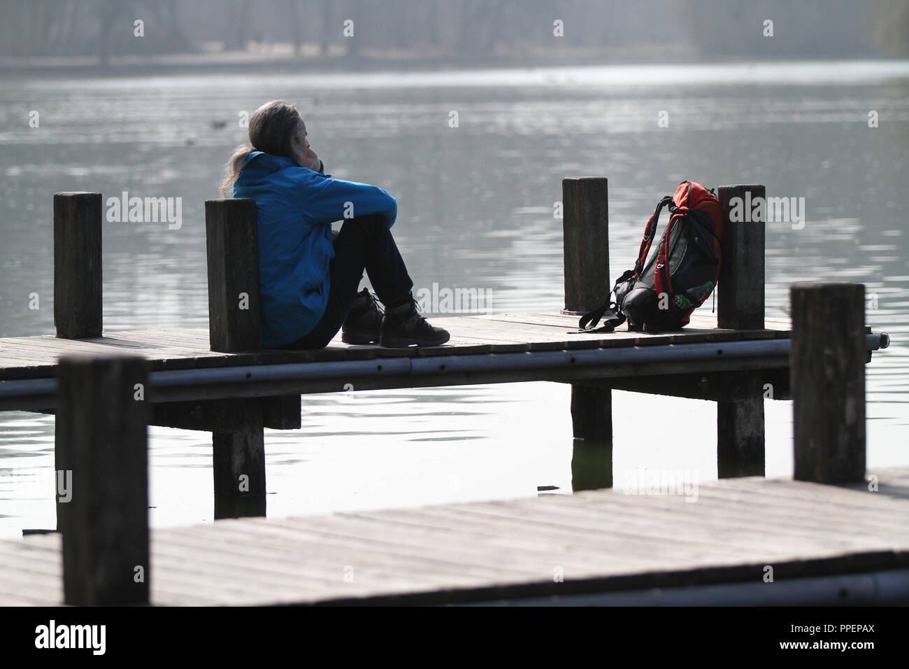 Un homme assis à l'embarcadère sur le lac Kleinhesseloher dans le jardin anglais sur une journée ensoleillée en mars. Banque D'Images