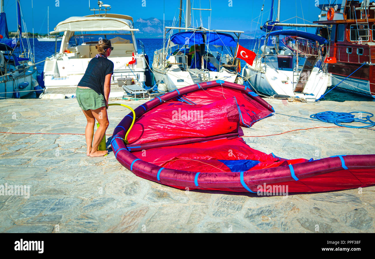 Datca/Turquie - 17 août 2018 : Kitesurfer pompage femme se remplit d'air son cerf-volant à l'aide de la pompe et des bateaux et la Méditerranée en arrière-plan Banque D'Images