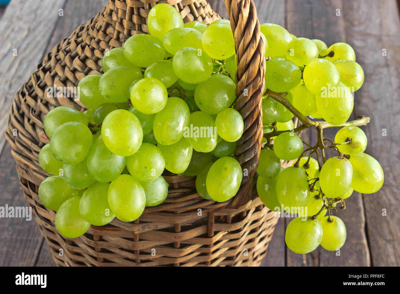 Raisin blanc avec sur la vieille bouteille de verre enveloppé en osier sur table en bois Banque D'Images