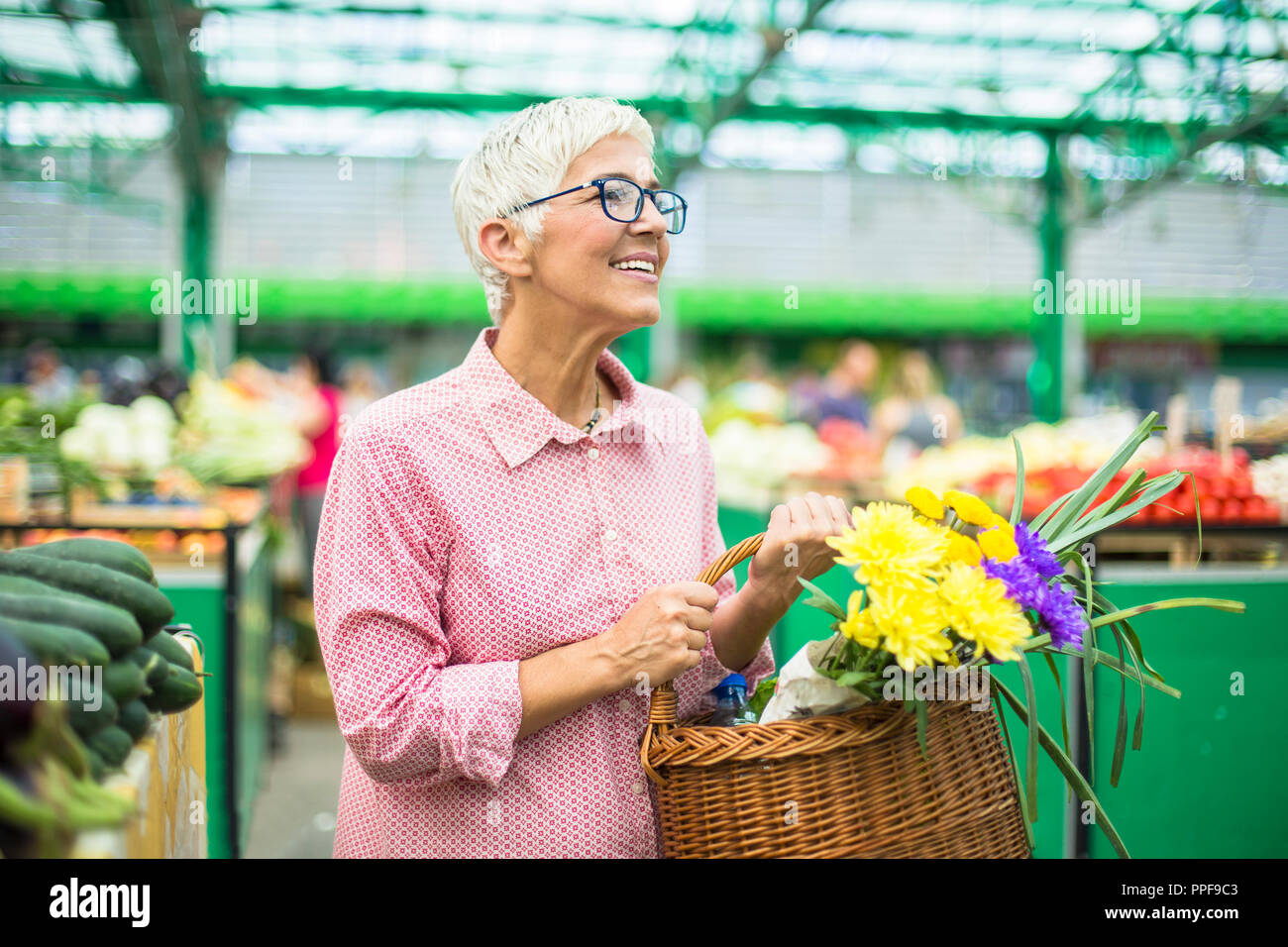 Portrait of senior woman holding basket avec bouquet de fleurs sur le marché intérieur Banque D'Images