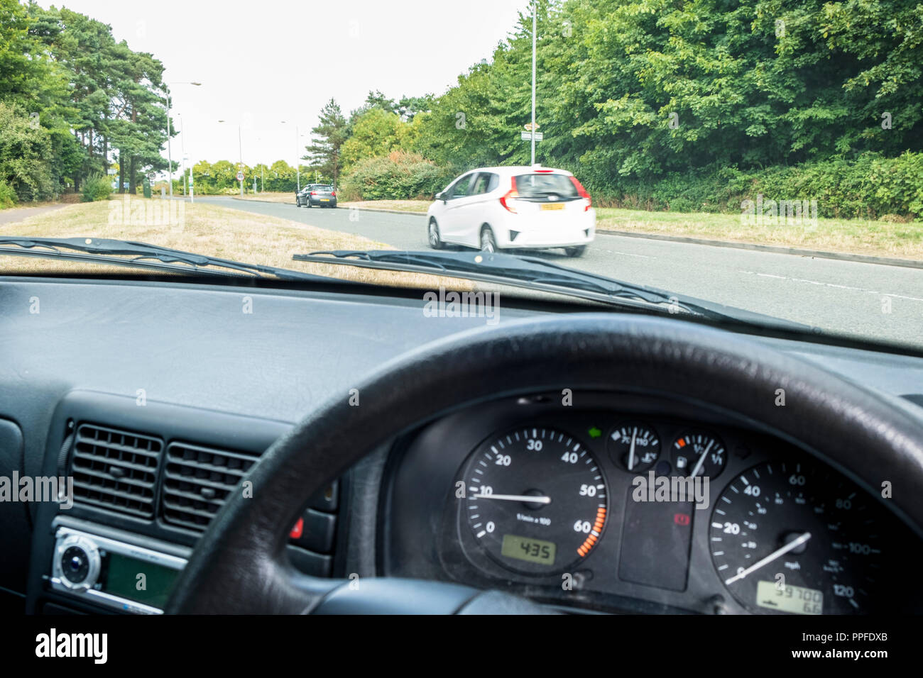 Voir l'observation à travers un pare-brise de voiture en attendant de tourner à gauche à une intersection, vu depuis le poste de conduite à l'intérieur du véhicule, England, UK Banque D'Images