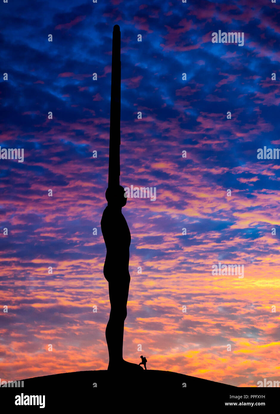 Une femme se tient aux pieds d'Antony Gormley's Angel de la sculpture du nord sous un ciel dramatique. Gateshead, England, UK. Banque D'Images