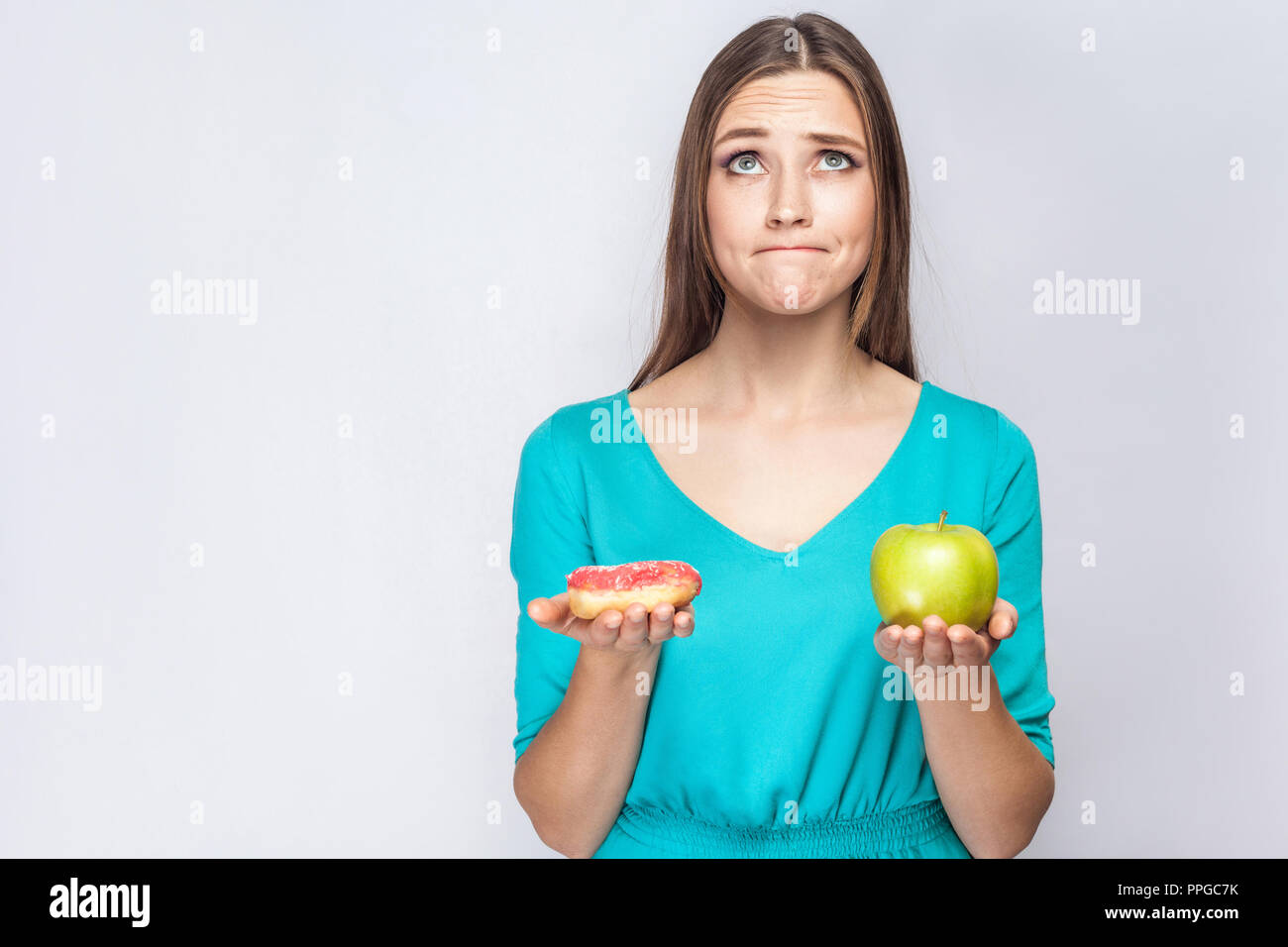 Portrait de jeune fille belle rêve en bleu, rose permanent chemisier holding donut et vert pomme dans les mains comme pesage avec thoughful face o Banque D'Images