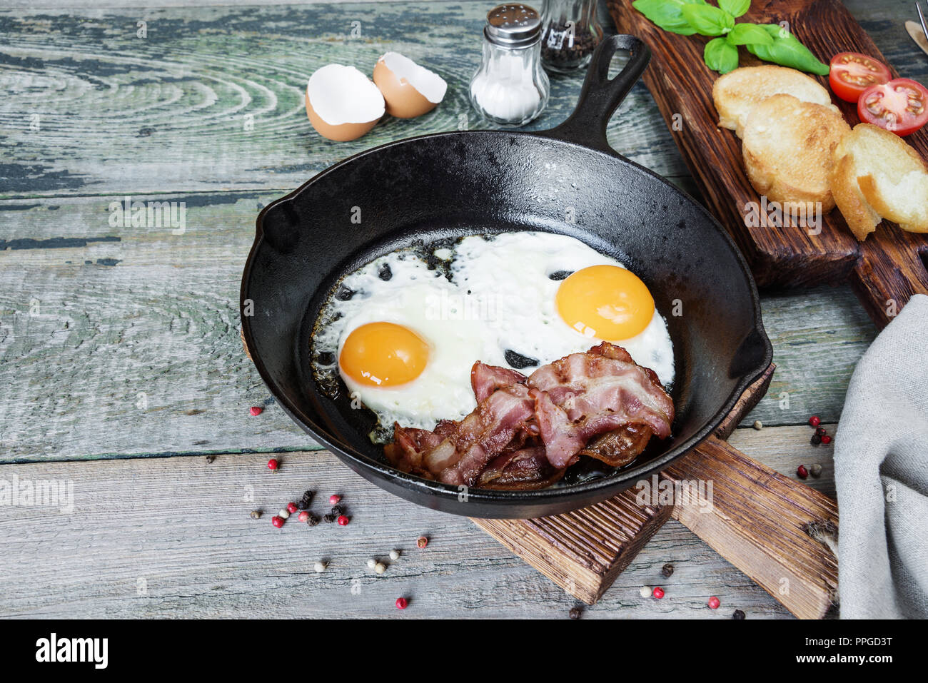Sur le plat, tranches de bacon, tomate et basilic de moitié dans une poêle en fonte sur une vieille table en bois dans un style rustique Banque D'Images