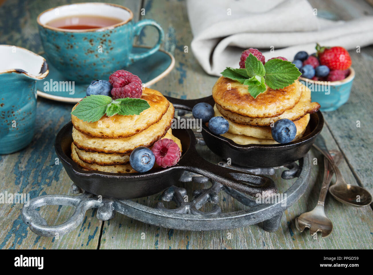 Petit-déjeuner de crêpes en fonte poêles, les baies fraîches et thé noir, dans un style rustique Banque D'Images