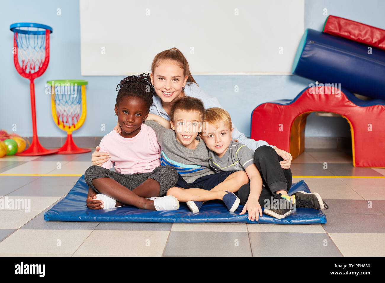 Trois enfants et leur enseignant de maternelle s'asseoir ensemble dans la salle de sport de la maternelle Banque D'Images