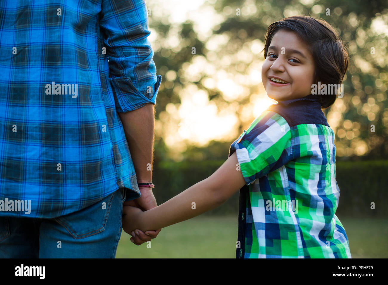 Vue arrière d'un happy boy holding hand de son père debout dans parc. Banque D'Images